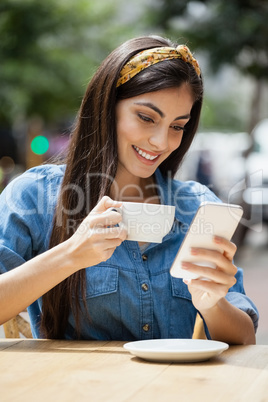 Woman using mobile phone while drinking coffee at cafe