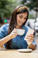 Woman using mobile phone while drinking coffee at cafe