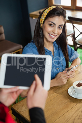 Owner holding tablet while woman sitting at table in coffee shop