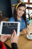 Owner holding tablet while woman sitting at table in coffee shop