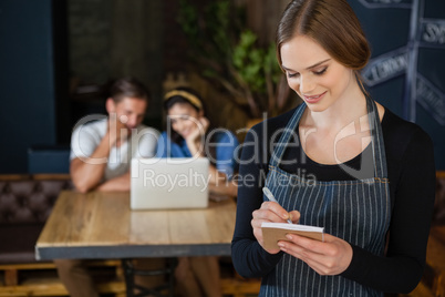 Smiling owner writing on notepad while standing against customer
