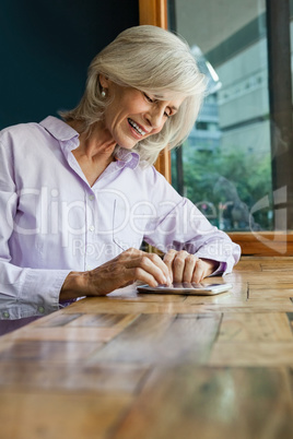 Smiling senior woman using smart phone while sitting at table