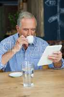 Senior man using tablet computer while drinking coffee