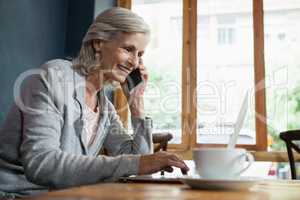 Smiling senior woman talking on mobile phone while working on laptop