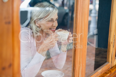 Smiling senior woman drinking coffee while sitting by table