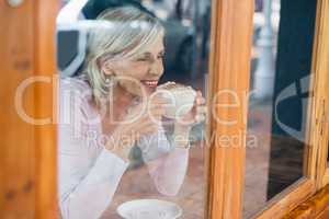 Smiling senior woman drinking coffee while sitting by table