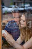 Happy couple holding smart phone while sitting at cafe