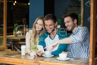 Happy friends looking at smart phone while sitting by table