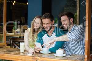 Happy friends looking at smart phone while sitting by table