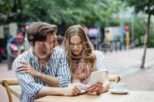 Cheerful couple holding mobile phone while sitting at sidewalk cafe