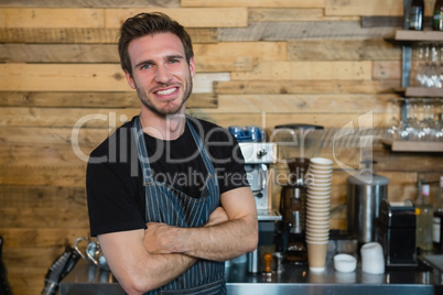 Portrait of smiling waiter standing with arms crossed