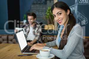 Portrait of young woman using laptop while having coffee