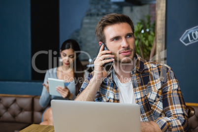 Young man talking on mobile phone while using laptop