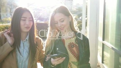 Two young women looking into smartphones on street