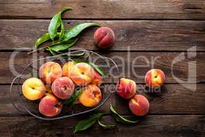 Fresh peaches fruits with leaves in basket on dark wooden rustic background, top view