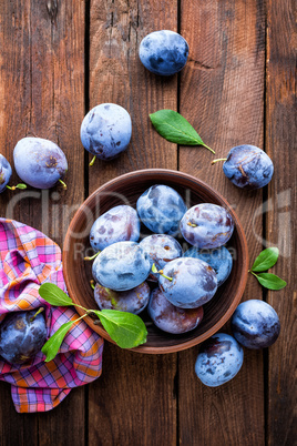 Fresh plums with green leaves on wooden rustic background, top view