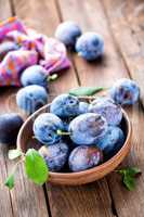 Fresh plums with green leaves on wooden rustic background