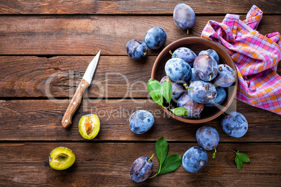 Fresh plums with green leaves on wooden rustic background, top view
