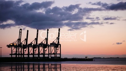 silhouetted tanker ship boat sailing into a port with cargo cranes at sunset or sunrise