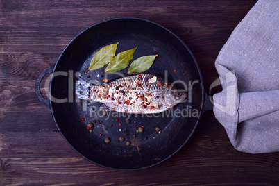 Crucian carp in spices on a black cast-iron frying pan