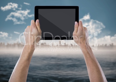 Hand with tablet against blurry skyline with water