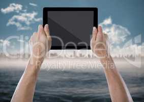 Hand with tablet against blurry skyline with water