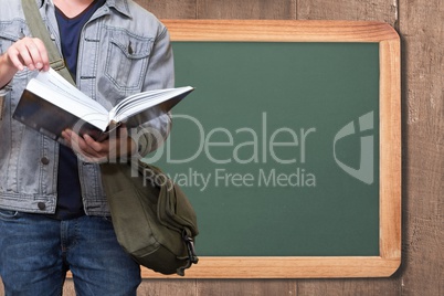 Midsection of man reading book while standing against board