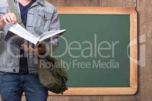Midsection of man reading book while standing against board
