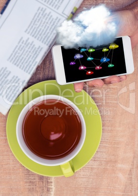 Overhead of hand with phone and tea and cloud with icons and flare