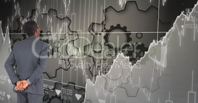 Digital composite image of businessman looking at graphs and gears on grid