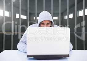 Criminal in hood with laptop behind prison bars
