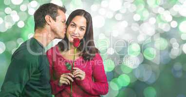 Portrait of woman holding rose while man kissing her over bokeh background