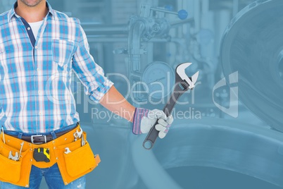 Midsection of worker holding wrench while standing against in factory