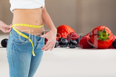 Midsection of woman measuring waist by fruits representing weight loss