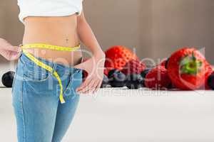 Midsection of woman measuring waist by fruits representing weight loss