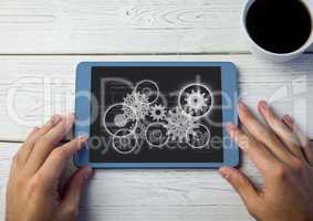 Overhead of hands with tablet and tea and white cog graphics