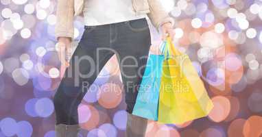 Midsection of woman holding shopping bags over bokeh