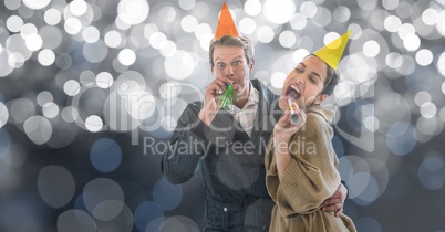 Happy couple blowing party horns against blur background