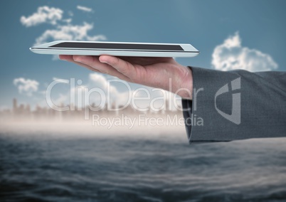 Hand with tablet against blurry skyline and water
