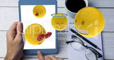 Digitally generated image of emojis flying over hand using tablet computer by cup at table