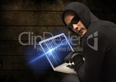 Criminal in hood on laptop in front of wood