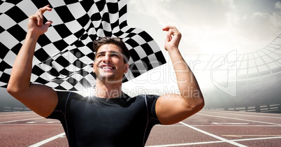Male runner with hands in air on track against flares and checkered flag