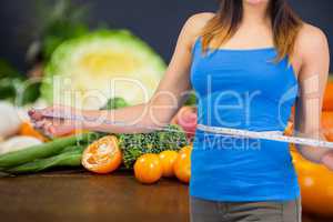 Midsection of woman measuring waist with vegetables in background