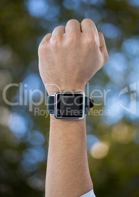 Fist in air with watch against blurry leaves