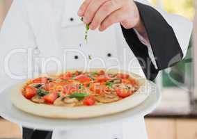 Chef pouring oregano to the pizza, foreground. Kitchen background