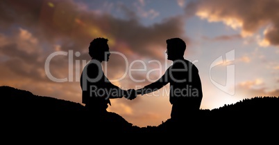 Silhouette business partners shaking hands on mountains during sunset