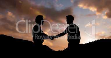 Silhouette business partners shaking hands on mountains during sunset