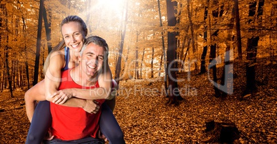 Fit man giving piggy back ride to woman in forest during autumn