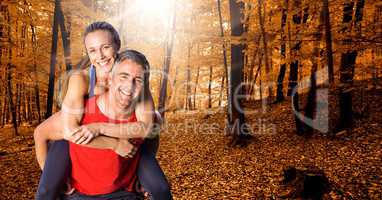 Fit man giving piggy back ride to woman in forest during autumn