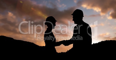 Silhouette professionals wearing hardhats while shaking hands